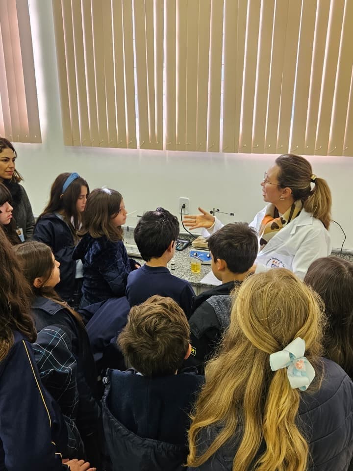 Alunos da escola em aula prática de laboratório, em bancada, com a professora acompanhando